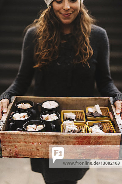 Midsection of happy woman carrying marshmallows drinks with chocolate crackers in serving tray