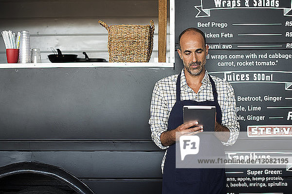 Male vendor using tablet computer while standing against food truck