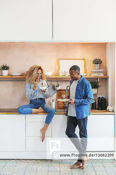 Full length of multi-ethnic couple eating salad and sandwich in kitchen