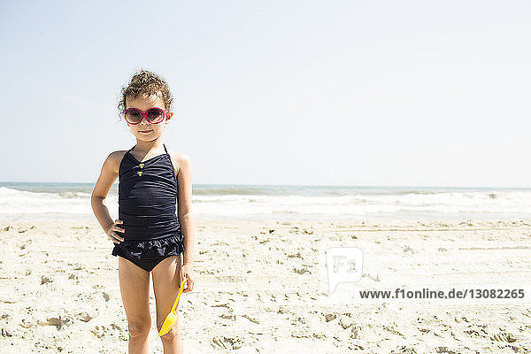 Portrait of girl in swimwear wearing sunglasses standing at beach during sunny day