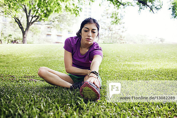 Entschlossene Sportlerin berührt die Zehen  während sie im Park auf Gras sitzt