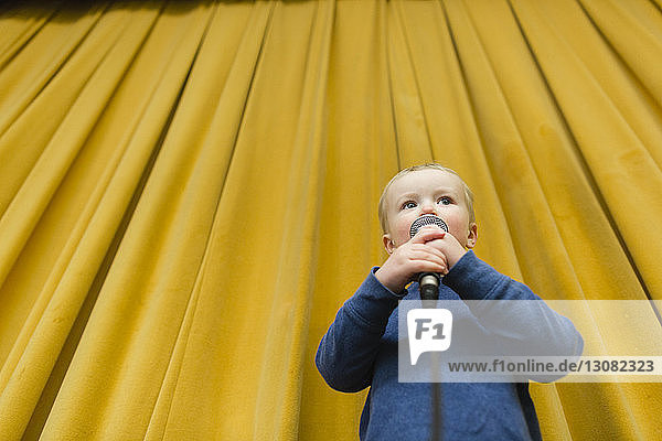 Niederwinkelansicht eines süßen Jungen  der auf der Bühne vor gelben Vorhängen am Mikrofon singt
