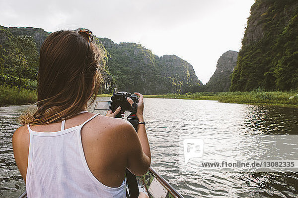 Rear view of woman photographing while traveling in boat on river