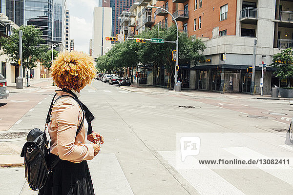 Seitenansicht einer Frau mit Tasche  die an einem sonnigen Tag auf der Stadtstraße steht