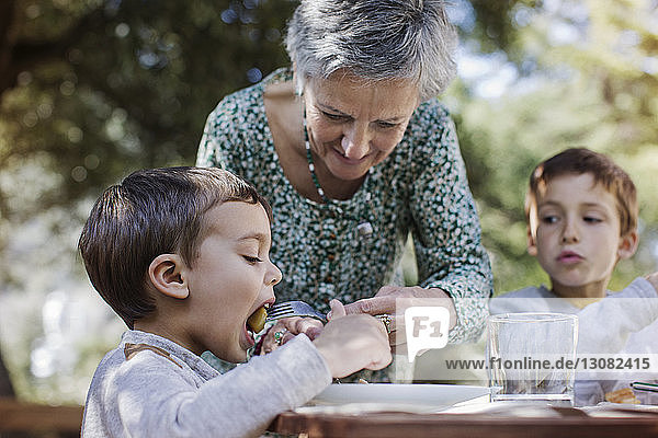 Ältere Frau füttert Enkel mit Frühstück auf dem Hof