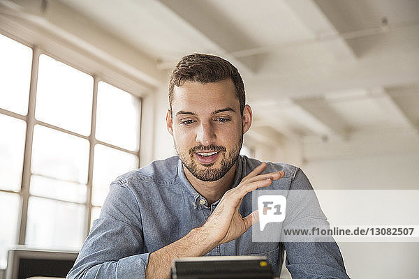 Glücklicher Geschäftsmann bei Videoanrufen im Büro sitzend
