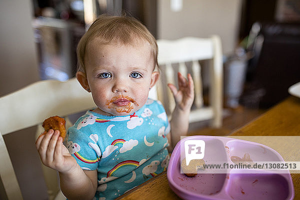 Portrait of cute baby girl eating food while sitting by table at home
