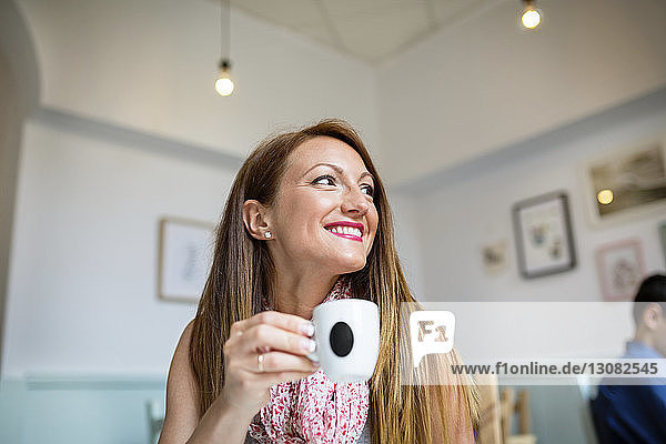 Glückliche Frau schaut weg  während sie eine Kaffeetasse im Café hält