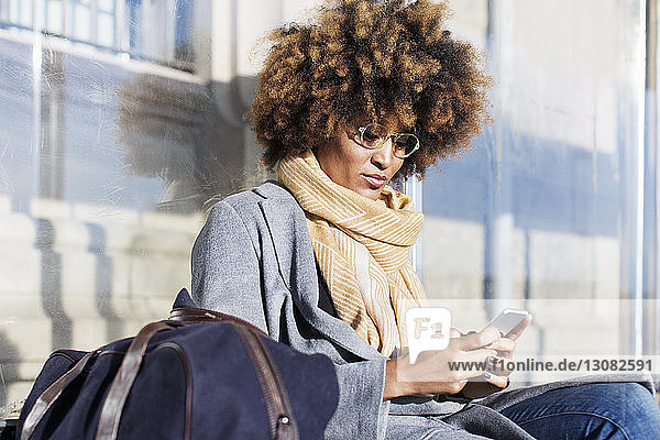 Frau benutzt Mobiltelefon  während sie an der Bushaltestelle sitzt