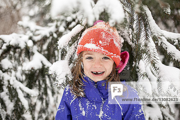Portrait of cheerful girl wearing warm clothing while standing against snow covered tree