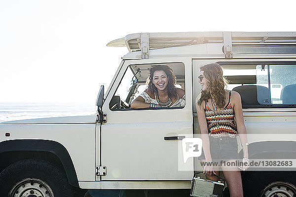 Happy woman looking at friend sitting in off-road vehicle during sunny day