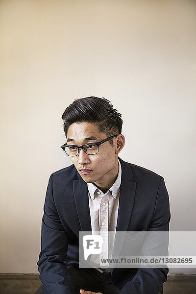 Thoughtful businessman sitting on chair against wall in office