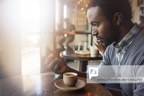 Thoughtful man holding mobile phone while sitting at table in cafe