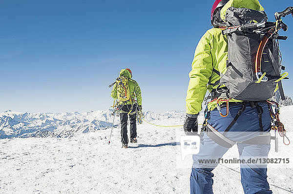 Rückansicht von Freunden mit Seil  die auf einem schneebedeckten Berg bei strahlend blauem Himmel laufen