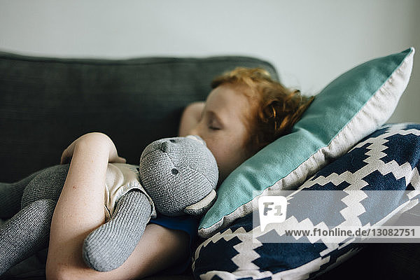 Seitenansicht eines Jungen  der zu Hause mit einem Teddybären auf der Couch schläft