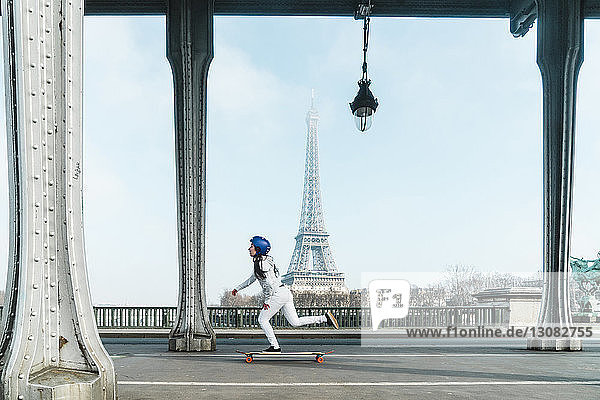 Seitenansicht einer Frau beim Skateboarden unter der Brücke gegen den Eiffelturm