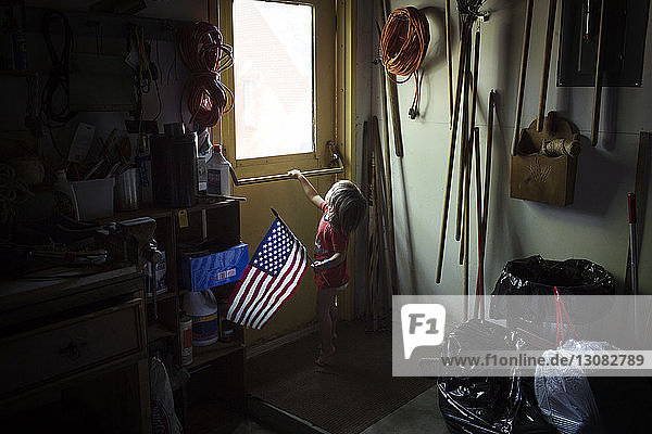 Junge hält amerikanische Flagge und schaut durchs Fenster