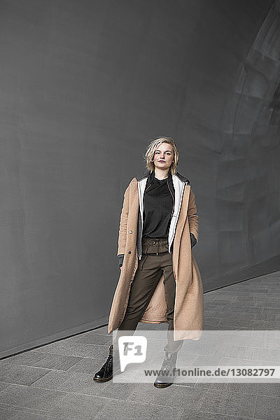 Porträt einer selbstbewussten Frau in voller Länge in der Nähe einer grauen Wand
