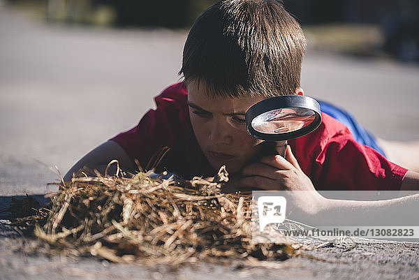 Boy with magnifying glass looking at grass while lying on road