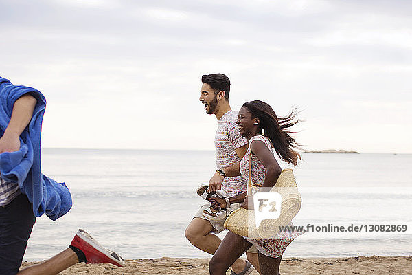 Seitenansicht von fröhlichen multiethnischen Freunden  die am Strand an Land laufen