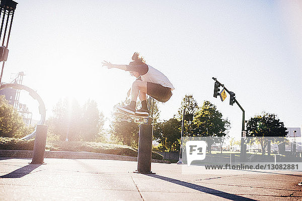 Mann führt Stunt mit Skateboard auf Stadtstraße gegen blauen Himmel bei Sonnenschein aus