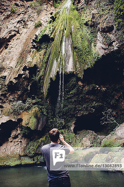 Rückansicht eines männlichen Wanderers  der den Wasserfall über Felsformationen betrachtet