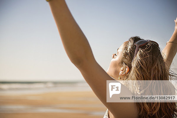 Seitenansicht einer sorglosen Frau  die am Strand die Arme hebt