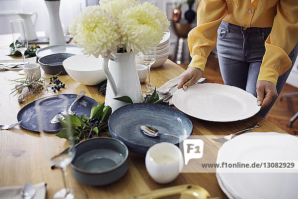 Close-up of woman arranging plates on table at home