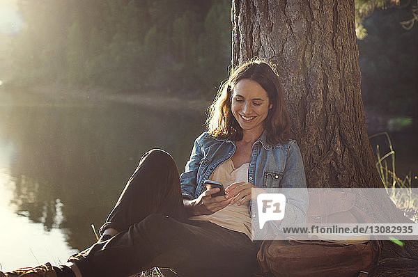 Smiling woman using mobile phone while relaxing at lakeshore