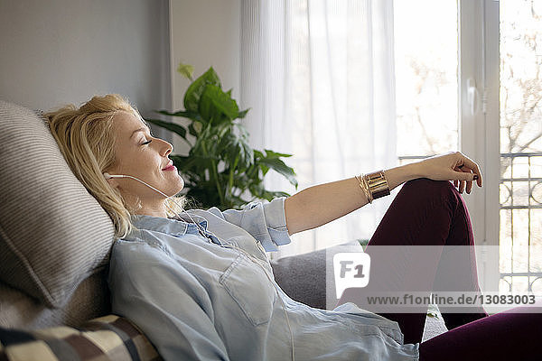 Side view of relaxed woman listening music while sitting on sofa at home