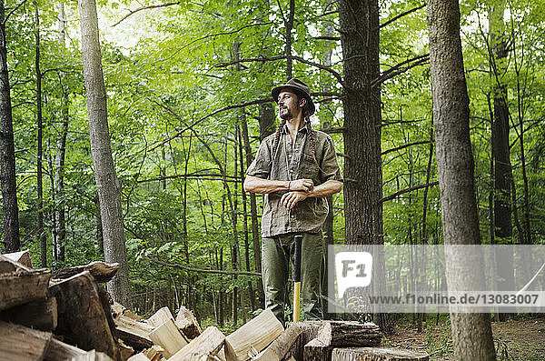 Happy man looking away while standing by firewood in forest