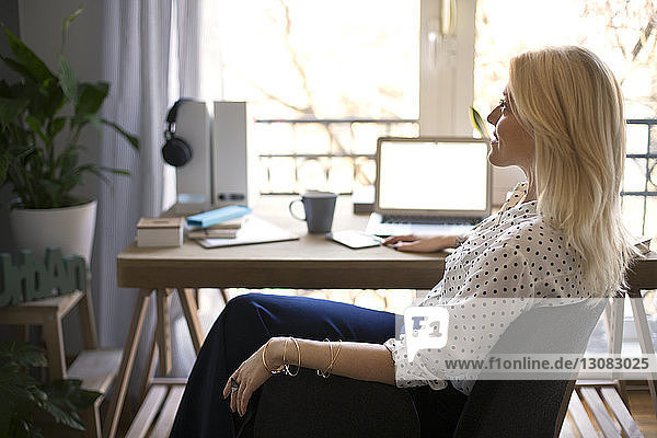Seitenansicht einer nachdenklichen Frau  die im Heimbüro auf einem Stuhl sitzt