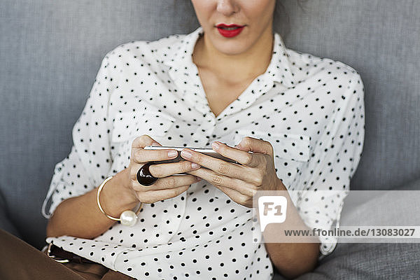 Midsection of businesswoman using smart phone at sofa in restaurant