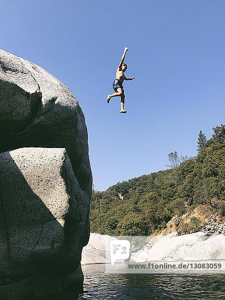 Low angle view of carefree shirtless boy jumping in Yuba River from cliff