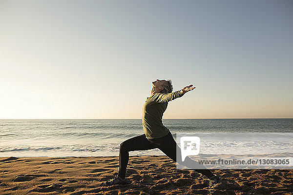 Seitenansicht einer Frau beim Yoga am Strand bei klarem Himmel