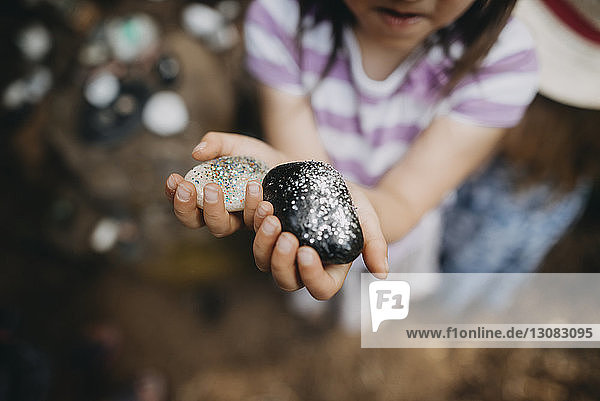 Midsection of girl showing decorated rocks with glitter