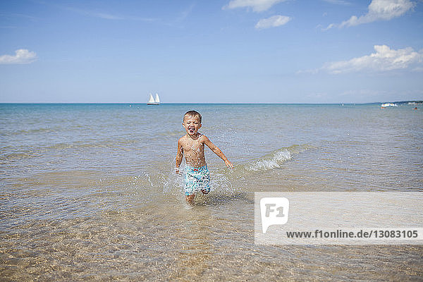 Fröhlicher Junge rennt an einem sonnigen Tag im Meer gegen den Himmel