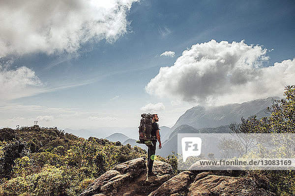 Seitenansicht eines männlichen Rucksacktouristen  der auf einem Berg vor bewölktem Himmel steht
