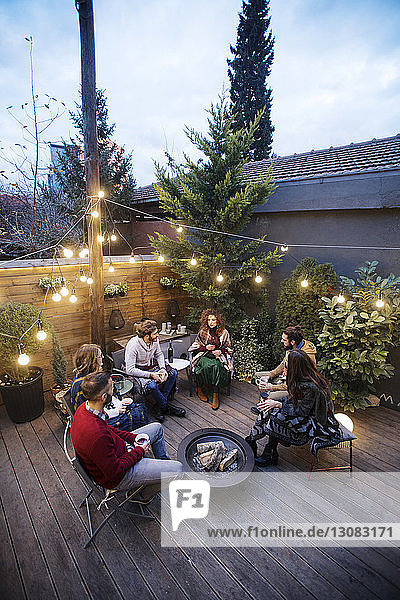 High angle view of friends enjoying drinks while sitting in backyard at dusk