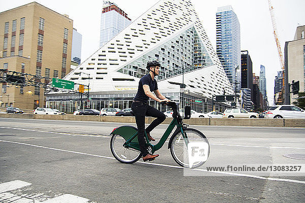 Fahrrad fahrender Mann in voller Länge auf der Straße bei Gebäuden in der Stadt