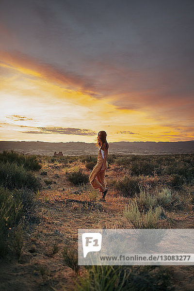 Seitenansicht einer Frau  die bei Sonnenuntergang vor bewölktem Himmel auf dem Feld geht