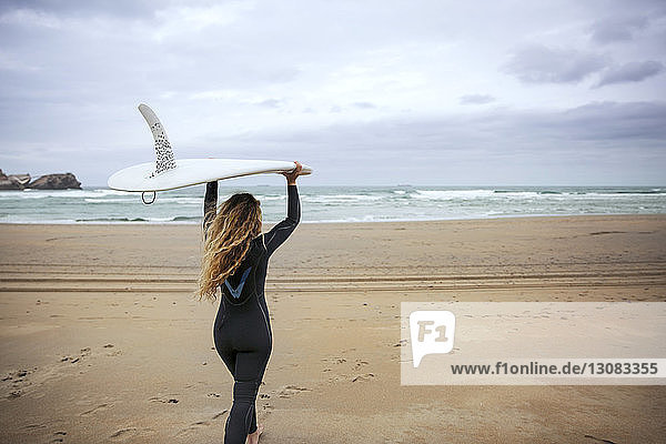 Frau trägt Surfbrett beim Spaziergang am Strand gegen den Himmel