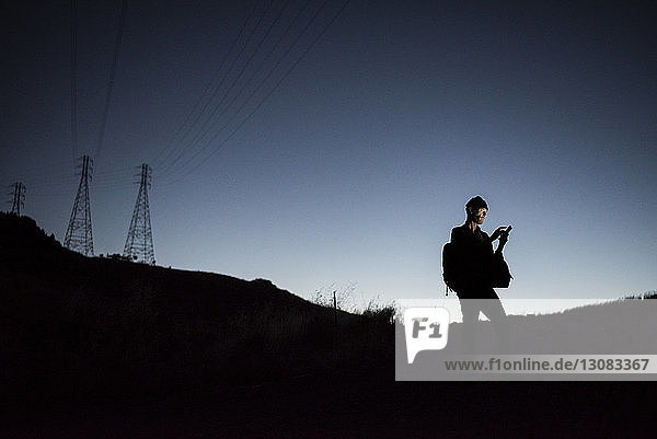 Mann benutzt Smartphone  während er in der Dämmerung gegen den klaren Himmel steht