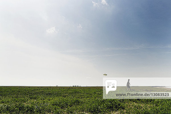Mann wirft fliegende Scheibe auf Grasfeld gegen den Himmel