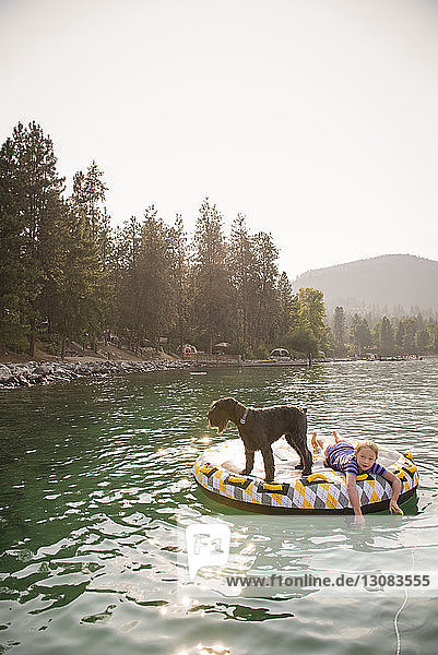 Mädchen mit Hund liegt auf einem Floß im See vor klarem Himmel