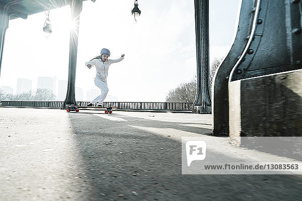 Skateboard fahrende Frau in voller Länge unter der Brücke gegen den Himmel