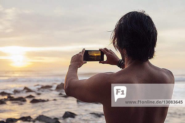 Rückansicht eines am Strand fotografierenden Mannes gegen den Himmel