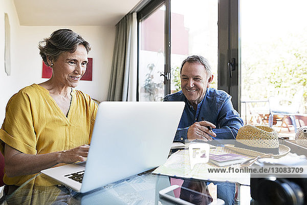 Glückliches älteres Ehepaar benutzt Laptop  während es seinen Urlaub zu Hause plant