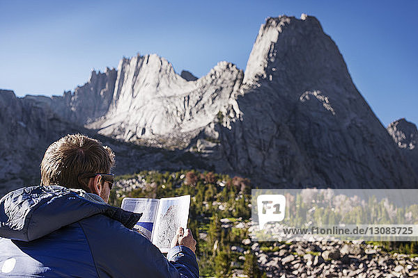 Rear view of hiker reading map against mountain