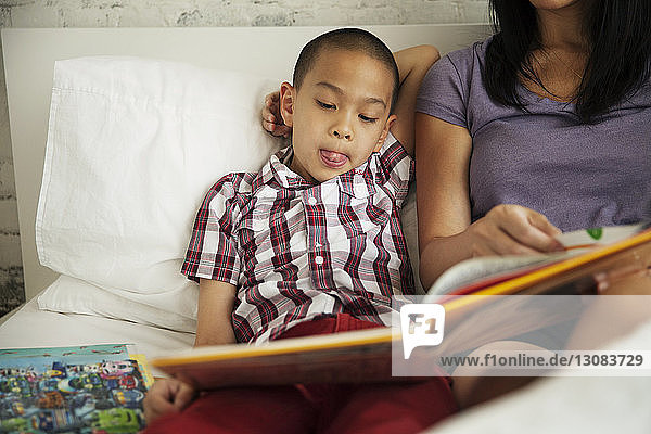 Boy listening to mother reading book on bed at home